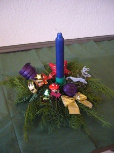 Auf Grünzeug dekoriertes 1er Gesteck mit langer, blauer Kerze zu 5,00 €.