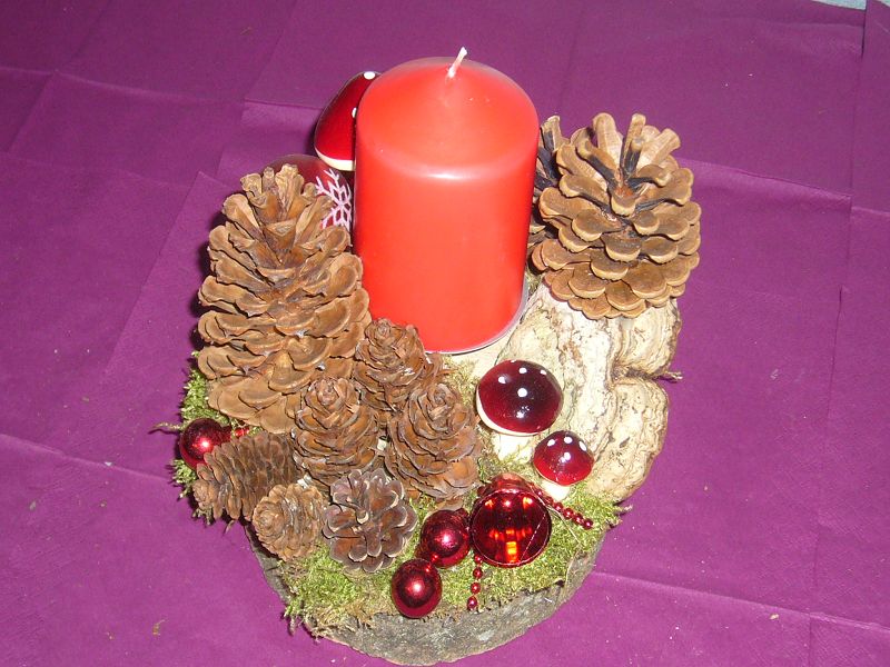 Rundliches 1er Gesteck auf Baumscheibe mit dicker, roter Kerze und Kiefernzapfen, ca. 20 cm im Durchmesser für 10,00 €.