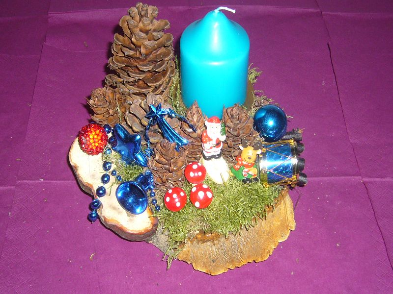 Rundliches 1er Gesteck auf Baumscheibe mit echtem Moos, Zapfen und Zaunblättling sowie blauer Kerze zu 8,00 €.